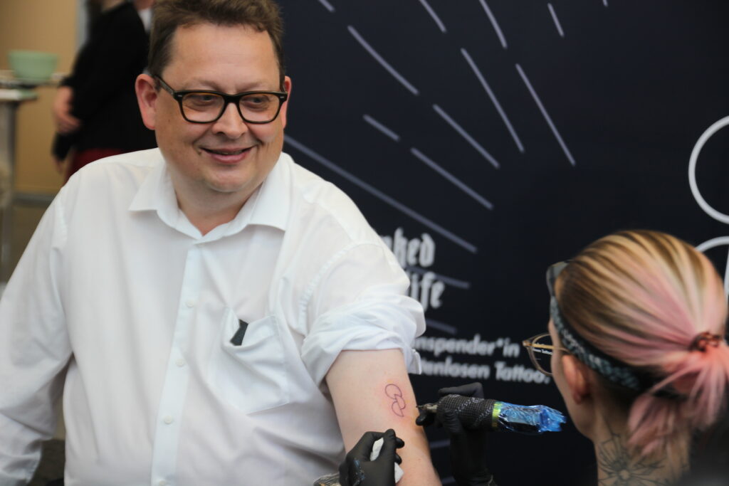 Stefan Schwartze lässt sich im Bundestag das Tattoo Opt.Ink stechen